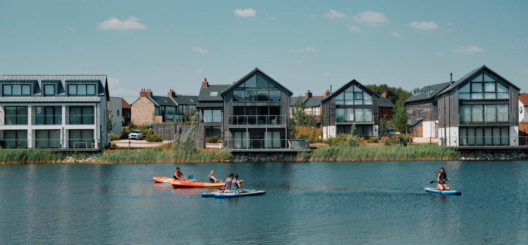 A family paddleboarding on a lake in front of some holiday homes