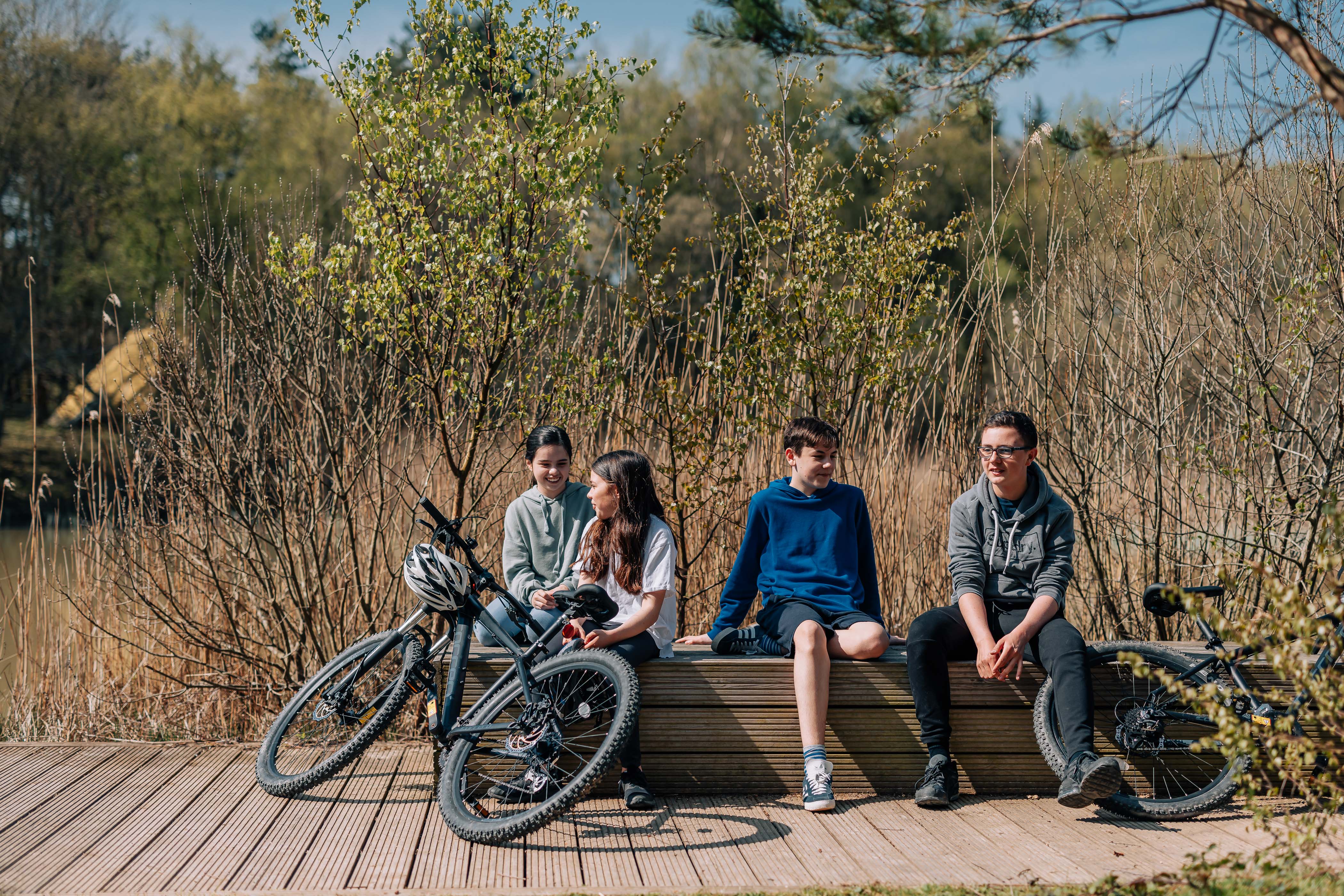 Four  young people sitting on a wall with shrubs in the background and their bikes at their feet