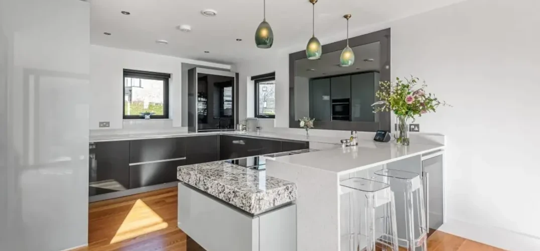 A white kitchen with marble worktops, grey cupboards and hanging lights