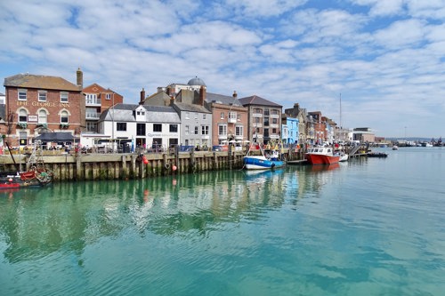 Colourful Weymouth Harbour with little boats on the calm waters and old buildings along the harbour wall